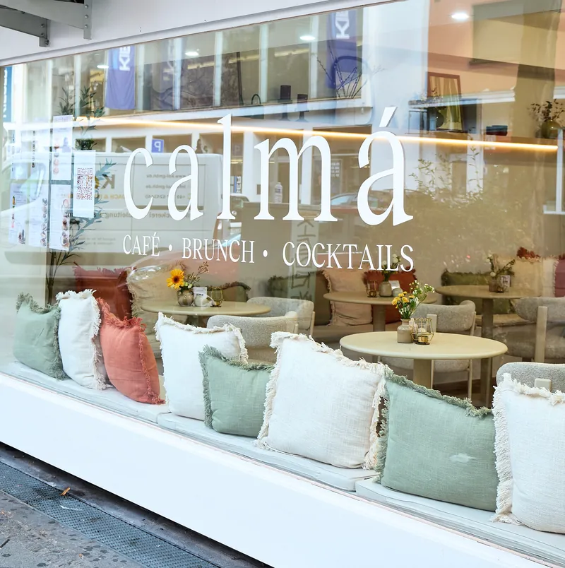 Schaufenster mit calmá-Schriftzug und Kissenbank hinter dem Glas