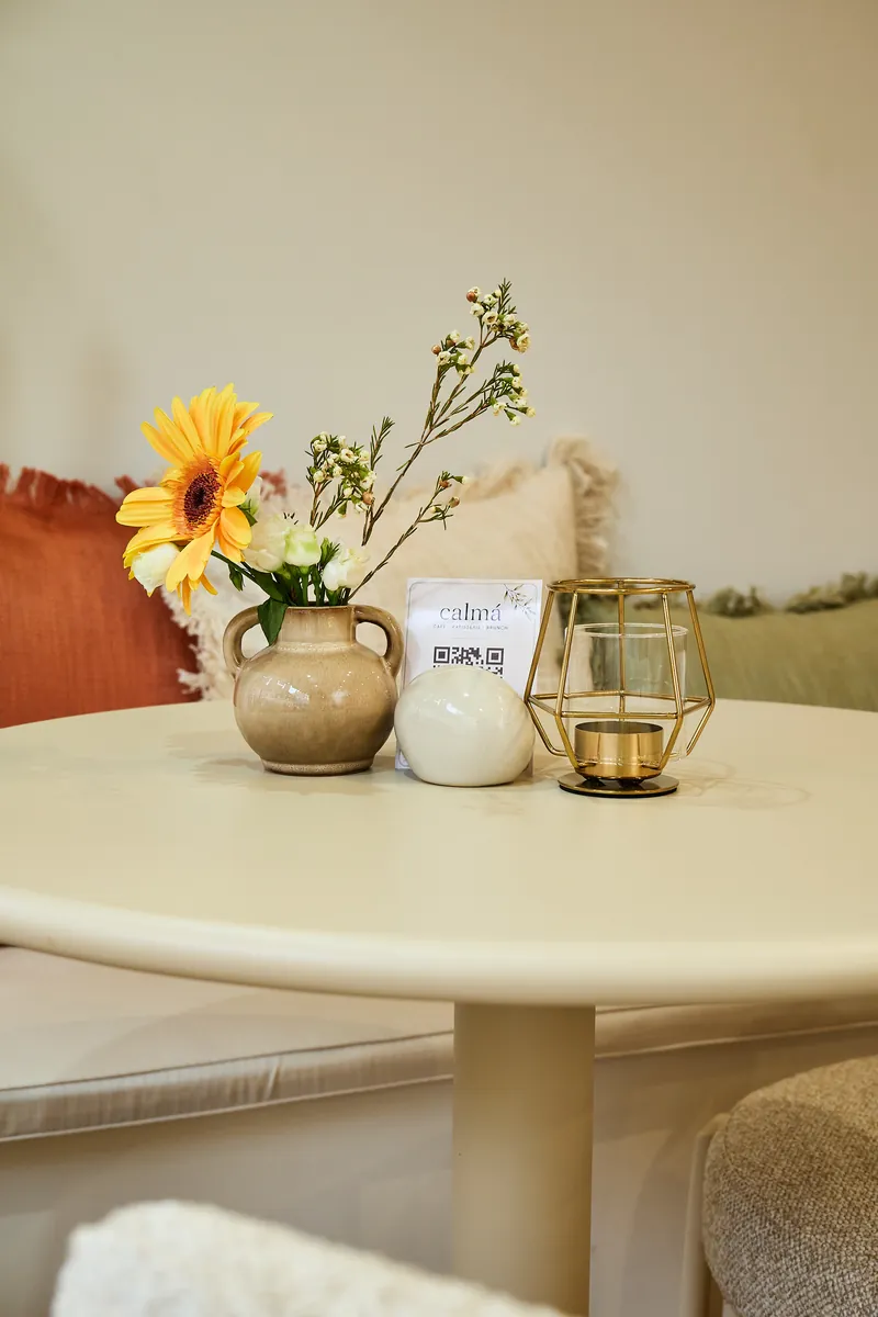 Tischdeko mit Gerbera im Krug, goldenem Windlicht und calmá-Tischkarte